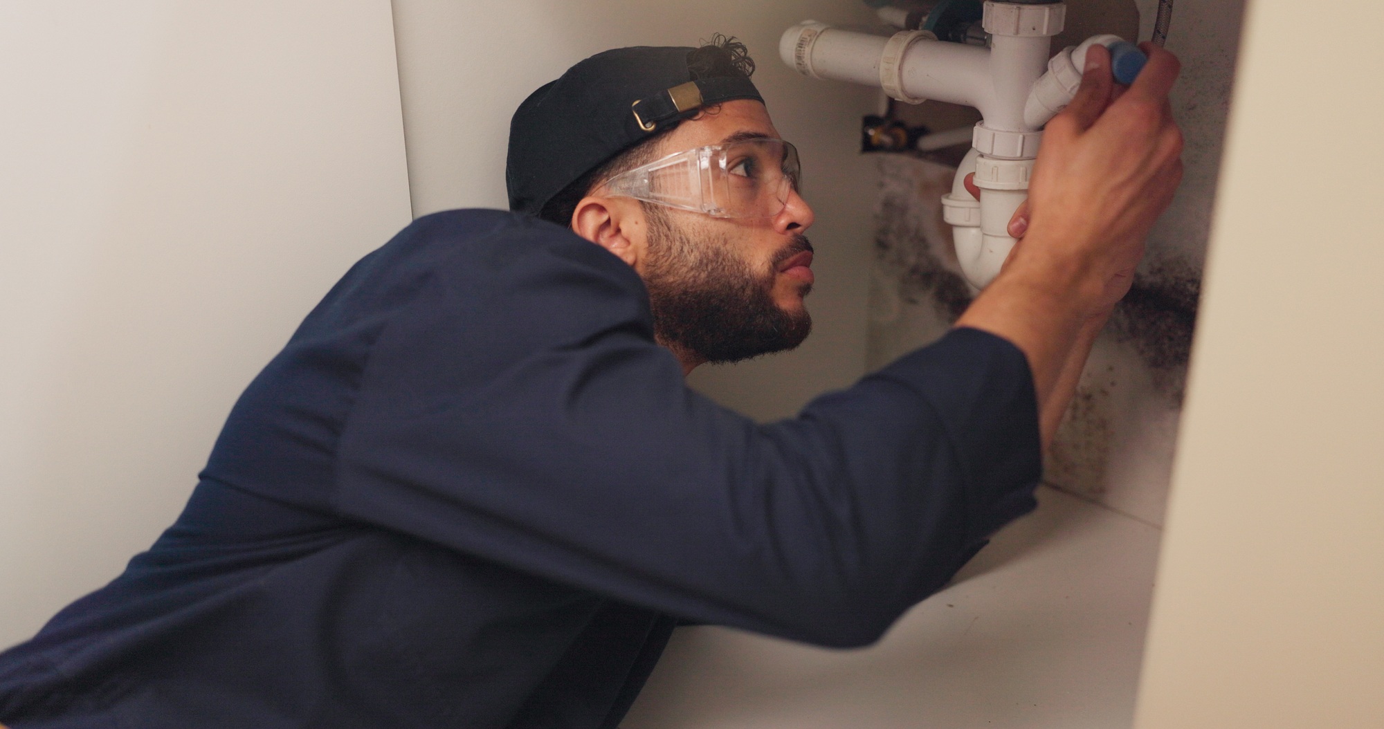 Plumber, man and pipeline repair in kitchen with tools for home maintenance and fixing leak by sink